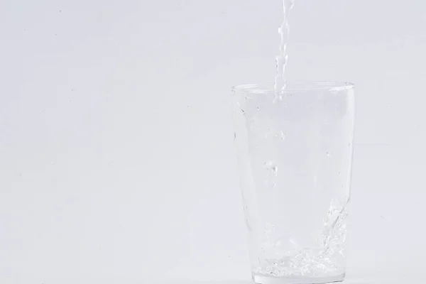 Вода льется в прозрачное стекло на белом фоне — стоковое фото