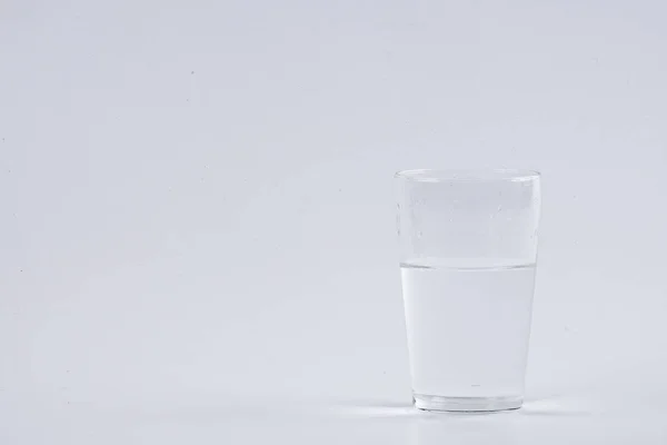 Voda proudí do čiré sklo nad bílým pozadím — Stock fotografie