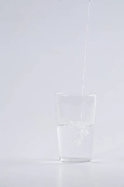 Woda lała się do szkło bezbarwne białe tło — Zdjęcie stockowe