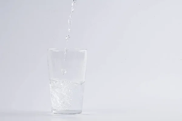 Acqua versando in vetro trasparente su sfondo bianco — Foto Stock