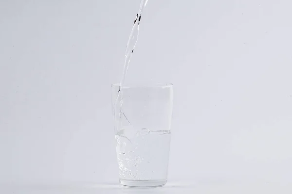 Água derramando em vidro transparente sobre fundo branco — Fotografia de Stock