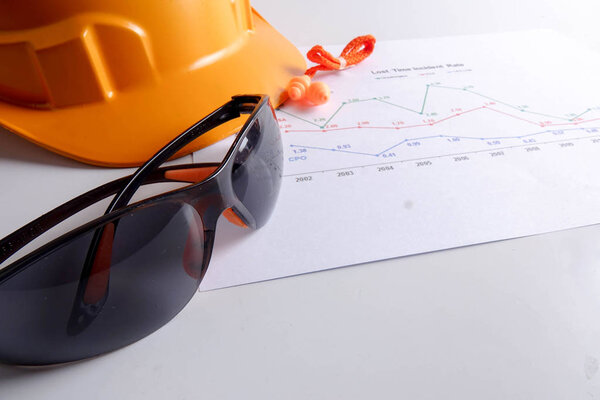 Yellow hardhat safety helmet,safety glass and ear plug over accident statistic graph as a background. Industrial safety and health conceptual.