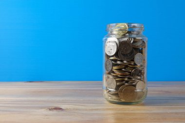 Mason kavanoza sikkeler üzerinde mavi arka ile bırakın. Kavram kaydetme.