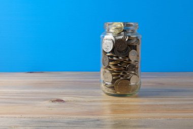 Mason kavanoza sikkeler üzerinde mavi arka ile bırakın. Kavram kaydetme.