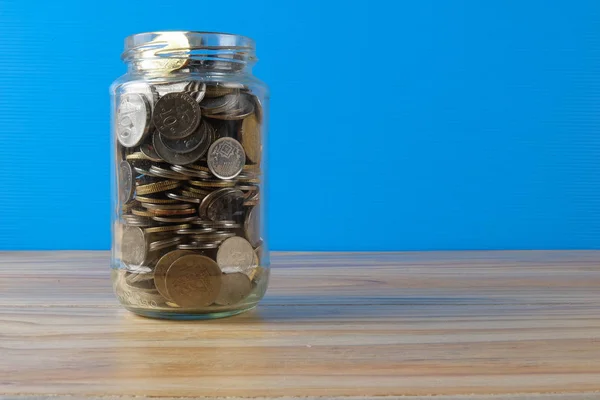 Mason jar with coins over blue back drop. Saving concept. — Stock Photo, Image