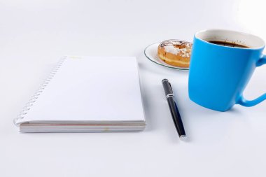 Not defteri ve kahve beyaz masaya çörek ile açıldı