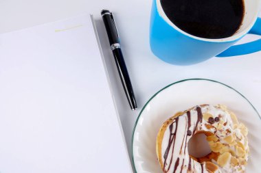 Not defteri ve kahve beyaz masaya çörek ile açıldı