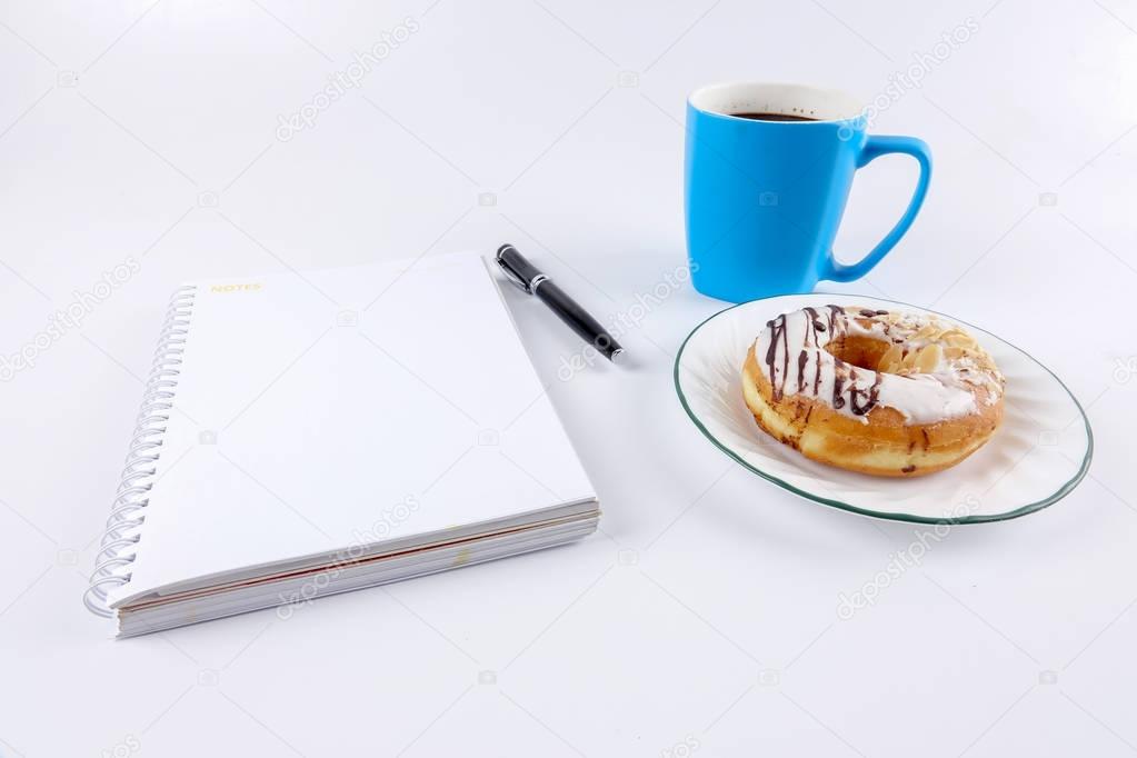 Opened notepad and cup of coffee with donut on the white table