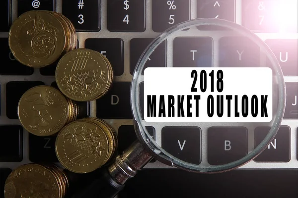 Magnify glass and coins on keyboard with 2018 MARKET OUTLOOK text. Business analysis concept.