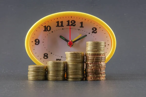 税の時間の概念 黄色の時計と黒の背景の上のコインの山 — ストック写真