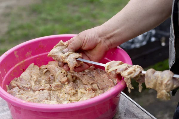 Bir adam ızgara ateşte et pişirmek için barbeküye çiğ domuz eti koyar.