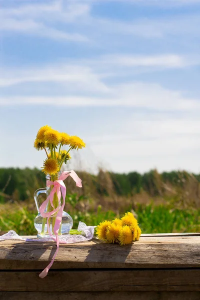 İlkbaharda, cam vazoda mavi gökyüzü zemininde güzel çiçekler. Arka planda şaşırtıcı sarı çiçek. Tahta bir yüzeyde