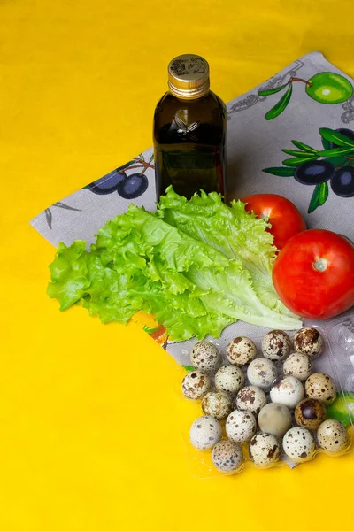 Dikey fotoğraf. Zeytinyağlı sağlıklı bir diyet salatası için bir set ürün. Bir şişe yağ, bıldırcın yumurtası, domates, marul, sarı arka planda sağlıklı yemek pişirmek.