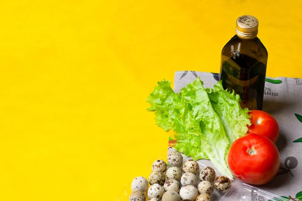 Zeytinyağlı sağlıklı bir diyet salatası için bir set ürün. Bir şişe yağ, bıldırcın yumurtası, domates, marul, sarı arka planda sağlıklı yemek pişirmek.