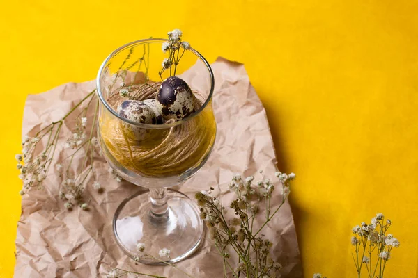 Bardakta iplikli küçük bıldırcın yumurtaları. Alışılmadık bir yemek fotoğrafı, sarı arka planda beyaz çiçekli eski kağıt üzerindeki cam..
