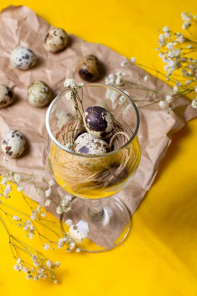 Dikey fotoğraf, iplikli küçük bıldırcın yumurtaları. Alışılmadık bir yemek fotoğrafı, beyaz çiçekli eski kağıt üzerindeki cam..