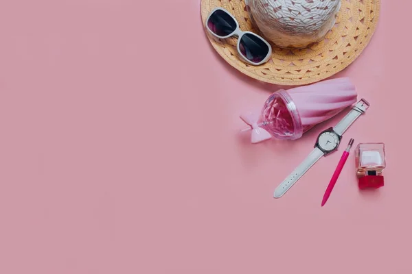 Üst görünüm güneş gözlükleri, şapka, pembe bardak, cam, tişört, kol saati, parfüm, kalem, yaz tatili ve tatil konsepti için pembe arka planda bir defter.