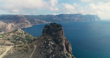 Mavi deniz, kum, gökyüzü, güneş ve bulutlu kayanın güzel hava 4k videosu. Sudak, Kırım.