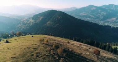 Güzel dağların ve tepedeki yeşil çayırların havadan görünüşü. Gün batımında dağlarda bir Verkhovyna köyünün insansız hava aracı çekimi, Karpat Dağları, Ukrayna.