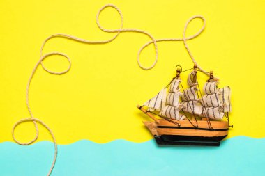 Oyuncak gemi mavi kağıt kesikli dalgalarda yüzüyor, halat sarı arka plandaki bir geminin üstündeki halkalar tarafından bükülüyor. Yazı kavrayın ve düz seyahat edin, taklit alanı oluşturun