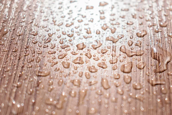 Water drops on a brown wooden table in the sun.Creative background,abstract texture.Selective focus,blurred background