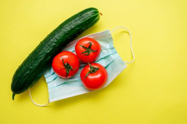 Üç domates ve salatalık sarı bir zemin üzerinde koruyucu bir tıbbi maskenin üzerinde yatıyor. Koronavirüs pandemiyle bağlantılı bir tarım krizi. Koronavirüs konseptini hasat edin.