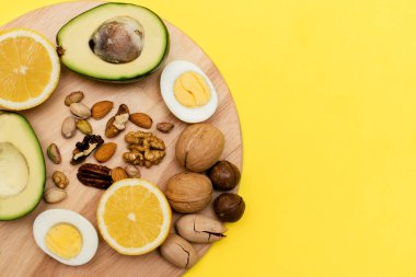 Düz ketojenik diyet. Vokado, yumurta, limon, sarı arka plandaki tahta kesme tahtasındaki fındık. Sağlıklı gıda kavramı. Makyaj için alanı kopyala