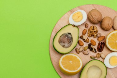 Düz ketojenik diyet. Vokado, yumurta, limon, yeşil arka plandaki tahta kesme tahtasındaki fındık. Sağlıklı gıda kavramı, üst görüş. Makyaj için alanı kopyala
