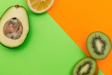 Düz ketojenik diyet. Yeşil ve turuncu arka planda vokado, limon ve kivi. Sağlıklı gıda kavramı, üst görüş. Makyaj için alanı kopyala