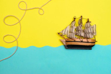Oyuncak gemi mavi kağıt kesikli dalgalarda yüzüyor, halat sarı arka plandaki bir geminin üstündeki halkalar tarafından bükülüyor. Yazı kavrayın ve düz seyahat edin, taklit alanı oluşturun