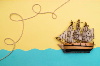 Oyuncak gemi mavi kağıt kesikli dalgalarda yüzüyor, halat sarı arka plandaki bir geminin üstündeki halkalar tarafından bükülüyor. Yazı kavrayın ve düz seyahat edin, taklit alanı oluşturun