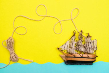 Oyuncak gemi mavi kağıt kesikli dalgalarda yüzüyor, halat sarı arka plandaki bir geminin üstündeki halkalar tarafından bükülüyor. Yazı kavrayın ve düz seyahat edin, taklit alanı oluşturun