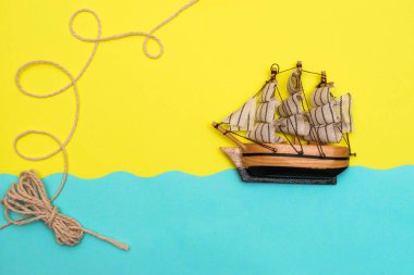 Oyuncak gemi mavi kağıt kesikli dalgalarda yüzüyor, halat sarı arka plandaki bir geminin üstündeki halkalar tarafından bükülüyor. Yazı kavrayın ve düz seyahat edin, taklit alanı oluşturun