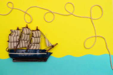 Oyuncak gemi mavi kağıt kesikli dalgalarda yüzüyor, halat sarı arka plandaki bir geminin üstündeki halkalar tarafından bükülüyor. Yazı kavrayın ve düz seyahat edin, taklit alanı oluşturun