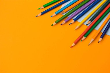 Okul konseptine geri dönelim. Renkli kalemler ve turuncu arkaplandaki defter. Yazı için boşluk kopyala, üst görünüm için.