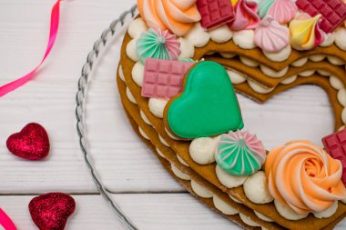 Doğum günü ve Sevgililer Günü için güzel bir tatlı. Kek, bembeyaz ahşap arka planda kırmızı kalpler ve kurdeleyle süslenmiş kalp şeklinde bir pasta.