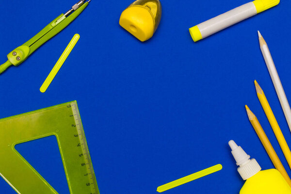 Back to school concept flat lay.Sharpener,ruler,color pencils,marker,compass,glue,counting sticks on the blue background.Copy space for text,top view