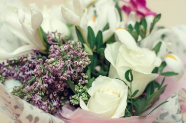 Beyaz gül buketi, beyaz süsen çiçekleri, leylak ve frezya hediye paketi beyaz tuğla arka planda. Sevgililer günü, doğum günü, düğün, anneler günü için hediye konsepti.