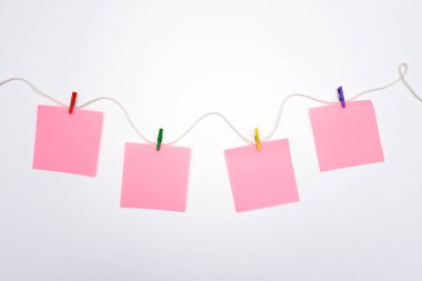 Pembe boş kağıt etiketleri beyaz bir arka planda renkli ahşap mandallarla bir ipe asılıyor. Not için boşluk kopyala