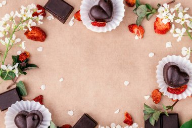 El yapımı çikolatalar, fındıklı dilimler ve tatlılar ve kağıt üzerinde kurutulmuş çilekler. Nane yaprakları, çilek dilimleri ve beyaz çiçekler arka plana saçılmış. Sağlıklı tatlılar.