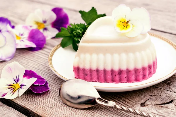 Souffle in the shape of a heart with cottage cheese, agar-agar and cream on a white plate on a wooden background.Violet flowers adorn the composition.oncept of healthy food and healthy dessert