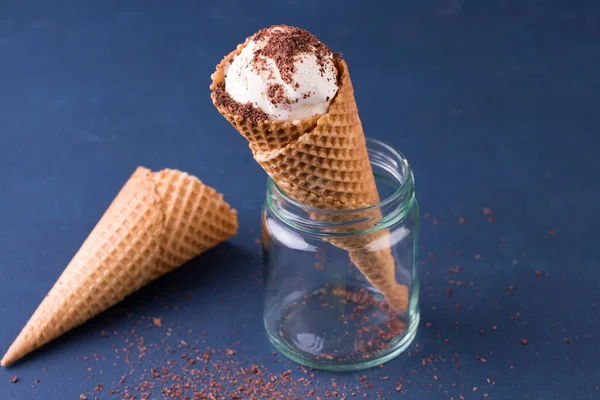 Traditional waffle cones for ice cream in glass jar on blue table. Cones filled with ice cream