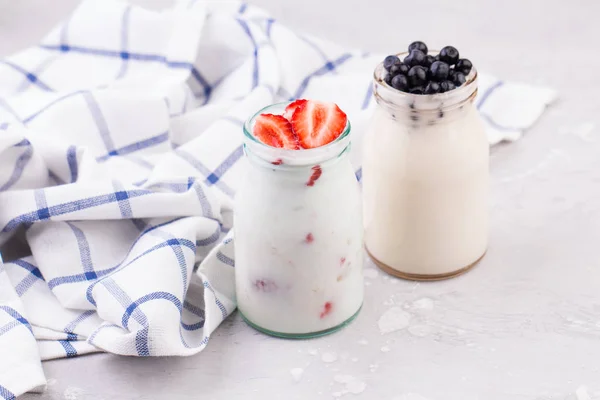 Los vasos de batido de leche con fresas y arándanos sobre una servilleta a cuadros azul sobre un fondo blanco — Foto de Stock