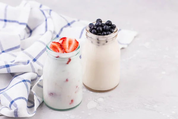 Los vasos de batido de leche con fresas y arándanos sobre una servilleta a cuadros azul sobre un fondo blanco — Foto de Stock