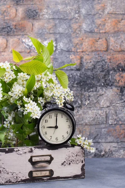 Alarm clock with spring blooming branch in wooden drawer against brick wall background. — Stock Photo, Image