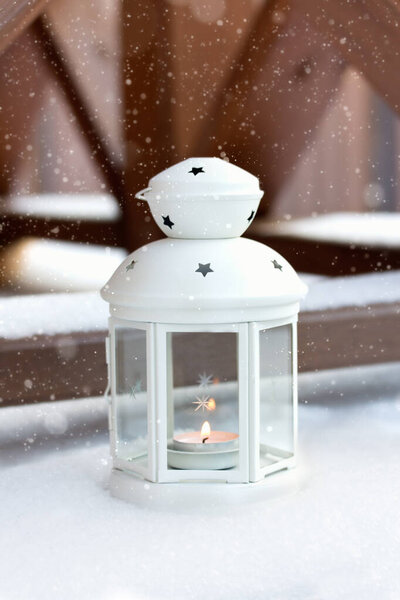 White Christmas lantern in snow, with yellow candle light, on wooden background