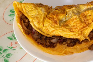 Omlet, masada beyaz bir tabakta servis edilen et ve soğanlı nefis bir omlet..