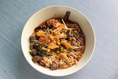 Birmanya eriştesi et, ciğer, kızarmış domuz, domates, mantar, biber ve diğer sebzeler bir tabakta servis edilir.