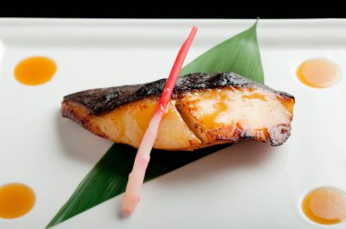 Limon çimi çubuğuyla kızartılmış siyah morina balığı ve beyaz bir tabakta bırakılmış. Gindara Teriyaki, soya soslu ızgara siyah morina balığı, beyaz arka planda izole edilmiş..