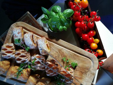Tahta üzerinde hamur işi olan vişneli domates ve kekik yaprakları. Vişneli domatesli kahvaltı pastası ve yukarıdan fesleğen. İçinde susam ve haşhaş tohumu olan ev yapımı simit sandviçleri..